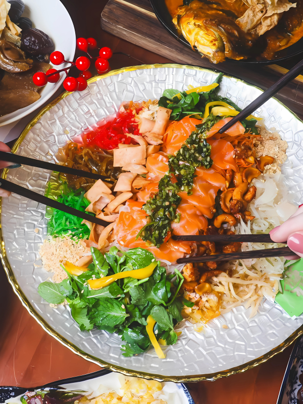 3 people feasting on yusheng in a lo hei restaurant Singapore.